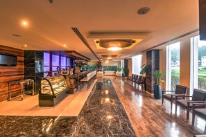 Un vestíbulo de hotel con piso de mármol, una recepción, zona de estar y amplias ventanas con vistas.