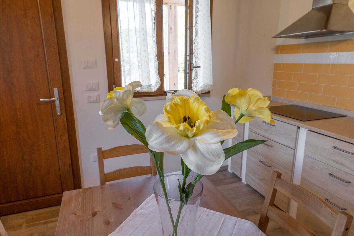 Uma cozinha com mesa de madeira, um vaso com flores e uma janela com cortinas.