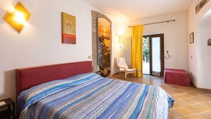 A bedroom with a large bed, a chair, and a small table. There is a window with curtains and a view of the outside. - Agriturismo San Giuseppe (Piombino)