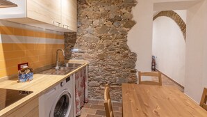 A compact kitchen with a stone wall, a washing machine, and a wooden dining table. - Agriturismo San Giuseppe (Piombino)