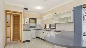 A kitchen with white cabinets, a built-in oven, and a curved countertop. - Cheerful beach house at redhead beach (Redhead)