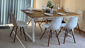A dining area with a wooden table set for six, white chairs, and a vase with flowers. - Cheerful beach house at redhead beach (Redhead)