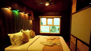 A room with a bed, wooden walls, a window, and a ceiling fan.