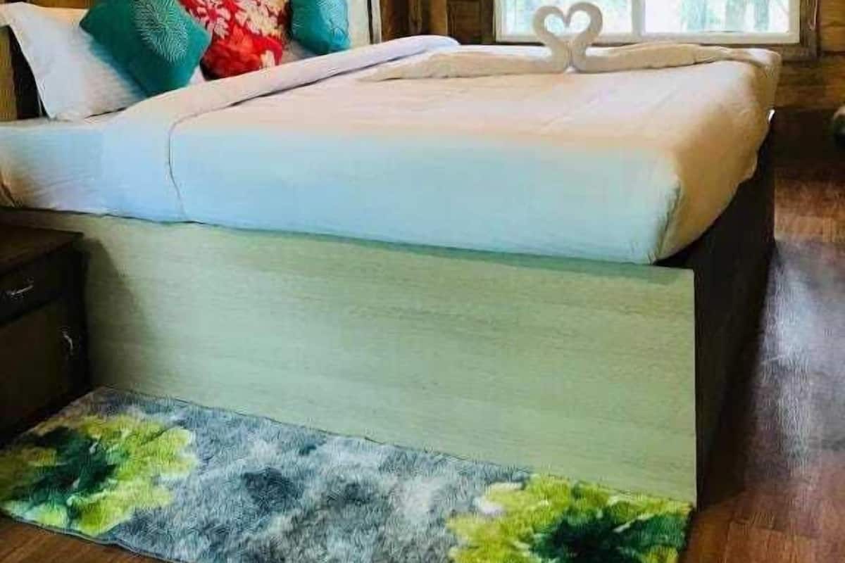 Quarto de cabana de madeira com cama, almofadas, janela e mesa de cabeceira.