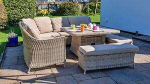 A wicker outdoor seating area with a sofa and ottoman, a table with plates, cups, and a teapot.