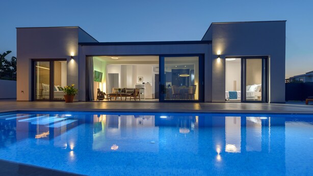 Ett modernt hus med en swimmingpool, stora glasdörrar och en väl upplyst interiör.