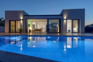 Ein modernes Haus mit Swimmingpool, großen Glasfenstern und einem hellen Innenraum.