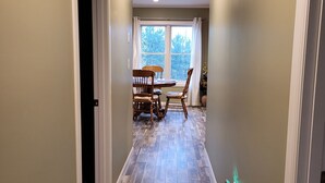 A hallway with a dining area at the end, featuring a table and chairs, and a window with a view of trees. - Guesthouse w/Heated garage/Fib intern/EV near MTU (Houghton)
