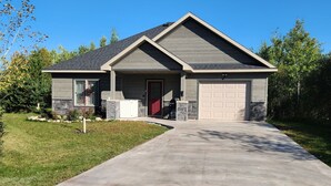 A modern single-story house with a grey roof, beige garage door, and a red front door. - Guesthouse w/Heated garage/Fib intern/EV near MTU (Houghton)