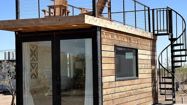 Una pequeña cabaña de madera con puerta de vidrio, una ventana y una escalera de caracol.