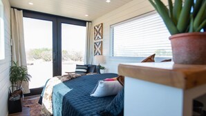 Un dormitorio con una cama, una silla, una planta en maceta y vistas al exterior.