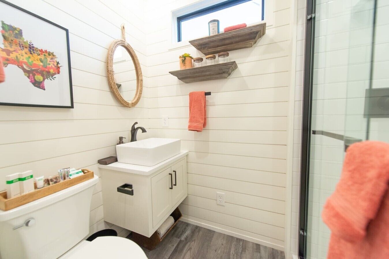 Une salle de bain avec un lavabo blanc, des toilettes, un miroir, un porte-serviettes et une fenêtre donnant sur un paysage agréable.