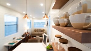 A modern interior with pendant lighting, a kitchen area with a wooden shelf, and a view of the sea.