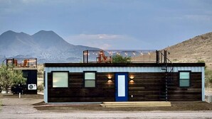 Une cabane en rondins moderne dotée d’un balcon, d’une porte et d’un petit espace extérieur aménagé pour s’asseoir.