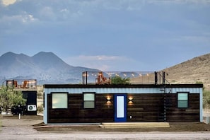 A modern log cabin with a balcony, a door, and a small outdoor seating area.