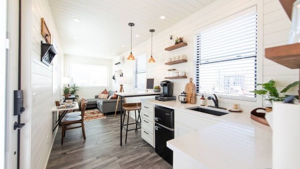 Une cuisine moderne avec un coin repas, un plancher en bois, des luminaires suspendus et une vue par la fenêtre.