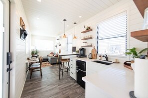 A modern kitchen with a dining area, wooden flooring, pendant lighting, and a view through the window. - The Longhorn Stunning Container Home-In Alpine (Alpine)