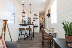 A compact kitchen with bar stools, a dining table, and a potted plant.