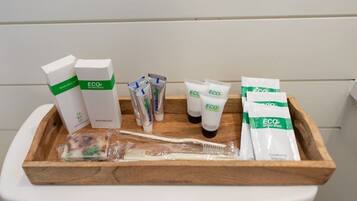 Un plateau en bois contenant un kit de rasage, un shampooing à la menthe fraîche et un après-shampooing, ainsi qu’une brosse à dents, posés sur les toilettes, qui sont de couleur blanche.