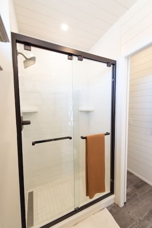 A glass-enclosed shower with a towel rack and a white tiled wall.