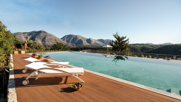 An infinity pool with a wooden deck, lounge chairs, and potted plants. - Nassibe (Mylopotamos)
