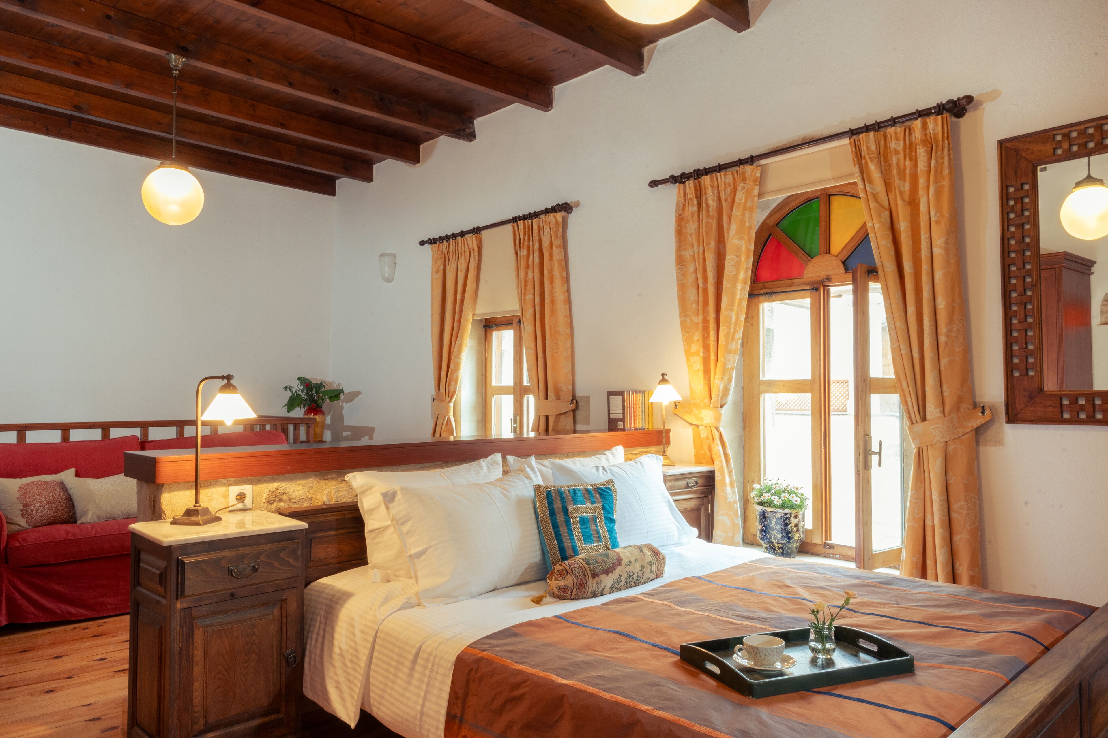A bedroom with a wooden bed, a nightstand, a red sofa, and a window with curtains.