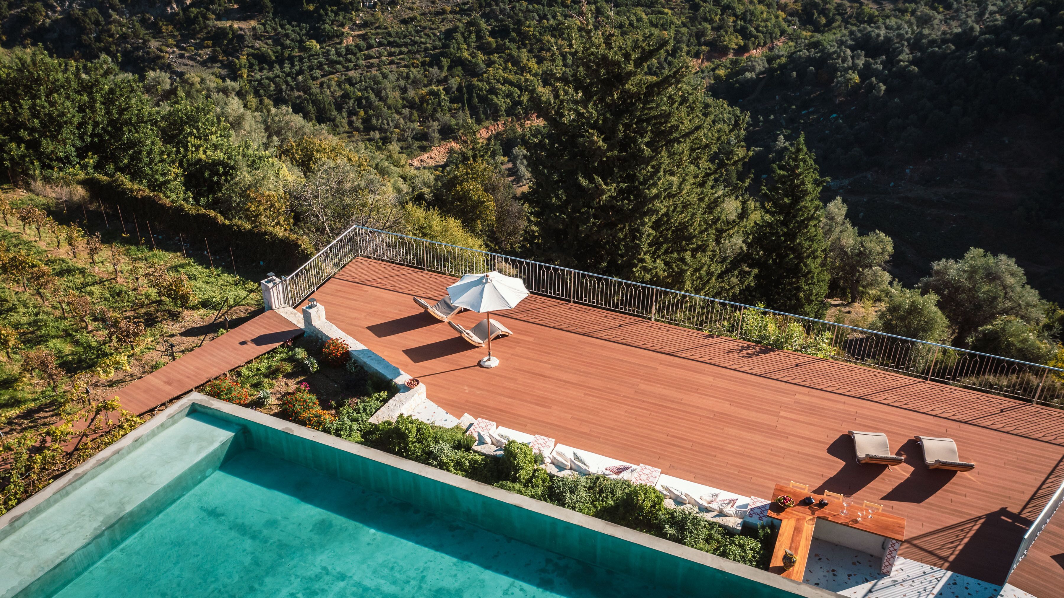 A rooftop pool area with a wooden deck, lounge chairs, and a table with outdoor seating.