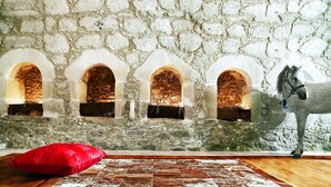 A room with a stone wall, three arched windows, a wooden floor, a red pillow, and a horse statue. - Nassibe (Mylopotamos)