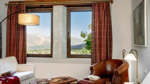 A hotel room with a large window, a sofa, a chair, a table with a tray, and a lamp. - Nassibe (Mylopotamos)