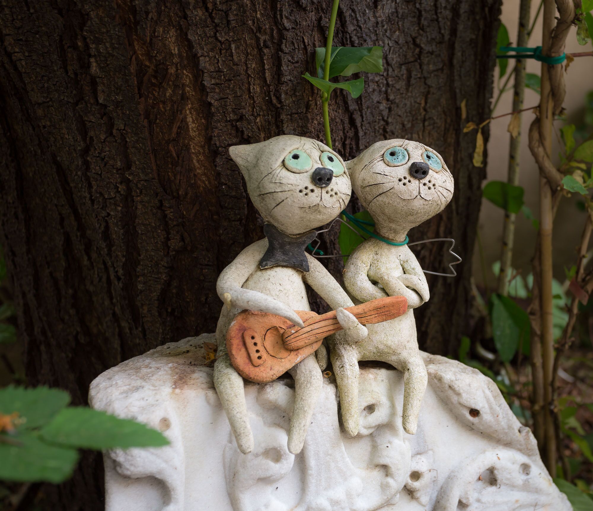 Two ceramic cat figures sitting on a rock with a tree in the background.