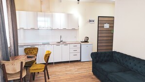 Un espacio habitable compacto con kitchenette, una zona de comedor con una mesa de madera y dos sillas, y un sofá verde oscuro.
