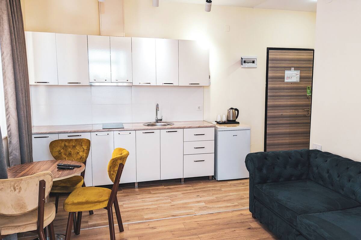 A compact living space with a kitchenette, a dining area with a wooden table and two chairs, and a dark green sofa.