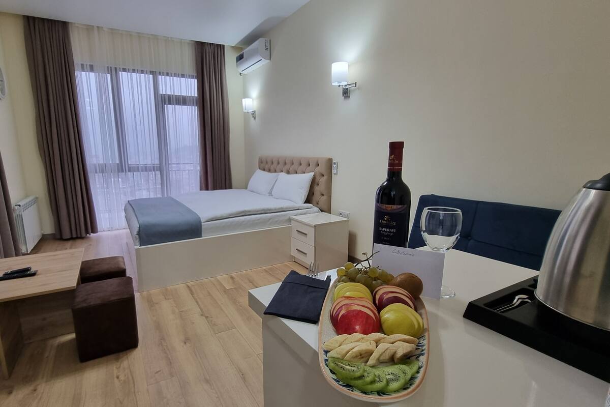 A hotel room with a bed, bedside table, desk, and a fruit basket.