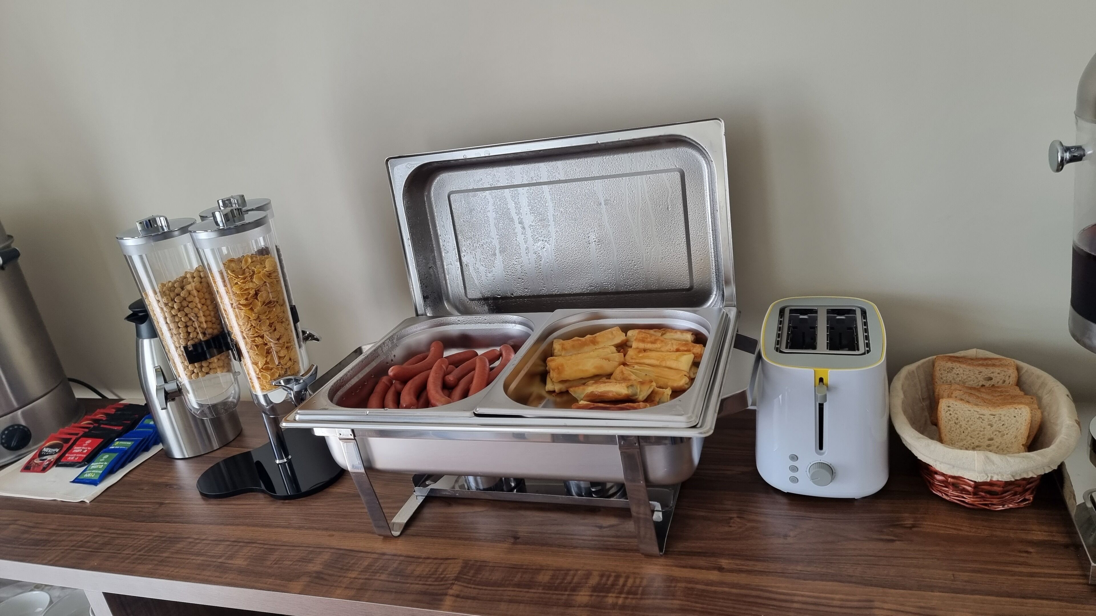 A buffet setup with a variety of food items including sausages, spring rolls, and cereal.
