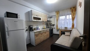 Eine kompakte Küche mit Kühlschrank, Mikrowelle und Herd. Es gibt einen Essbereich mit Tisch und einer Couch.