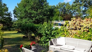 An outdoor patio with wicker furniture, a stone floor, and a view of a lush garden and trees. - Beautiful Quercy house near the Chemin de St Jacques (LUNAN)