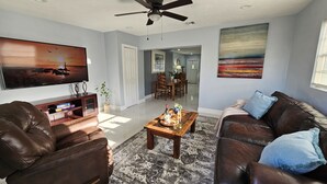 A living room with a television, leather sofas, a coffee table with drinks, and artwork on the walls. - Paradise Vacation Home for entire family (Boynton Beach)