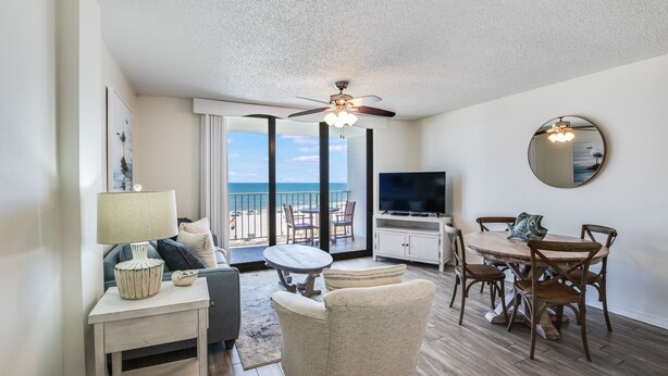 Un amplio salón con balcón con vistas al mar, una mesa de comedor y un televisor.