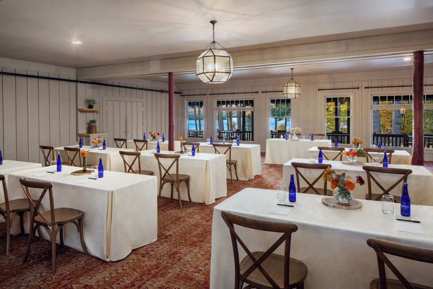 Une salle de banquet avec de nombreuses tables dressées pour le repas, agrémentée de nappes blanches, de verres bleus et de compositions florales.