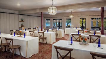 Une salle de banquet avec de nombreuses tables dressées pour le repas, agrémentée de nappes blanches, de verres bleus et de compositions florales.