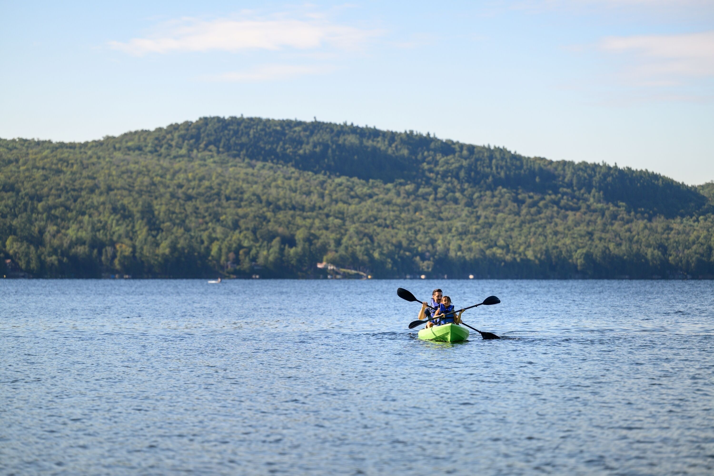 A kayak on a calm lake with a forested hill in the background.