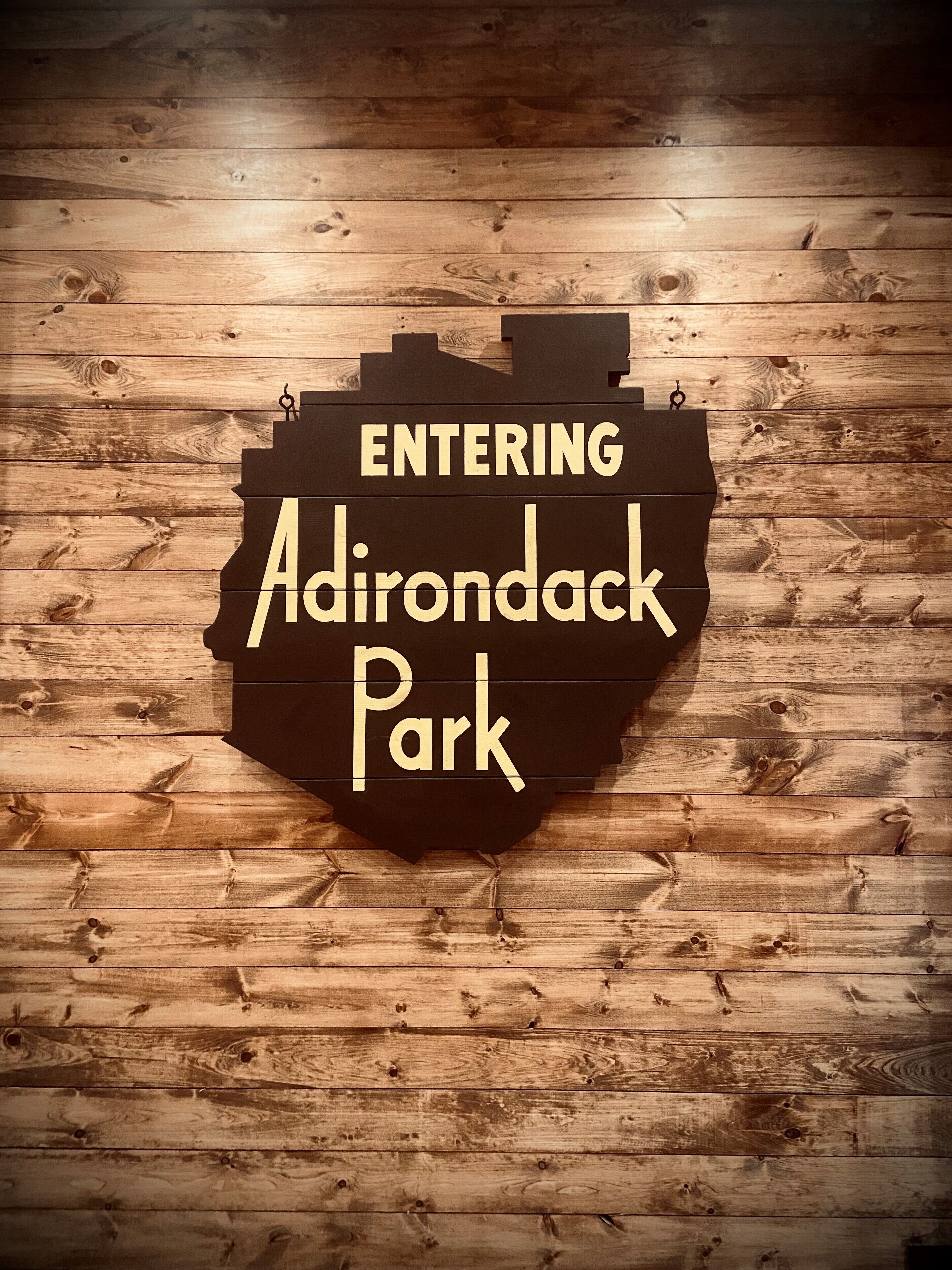 A sign with the text "ENTERING Adirondack Park" on a wooden background.