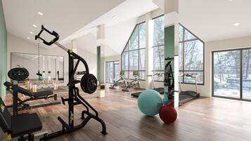 A spacious gym with various exercise equipment, large windows, and a wooden floor.
