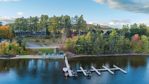 A lakeside property with docked boats, a stone pathway, and a view of the surrounding forest and buildings.
