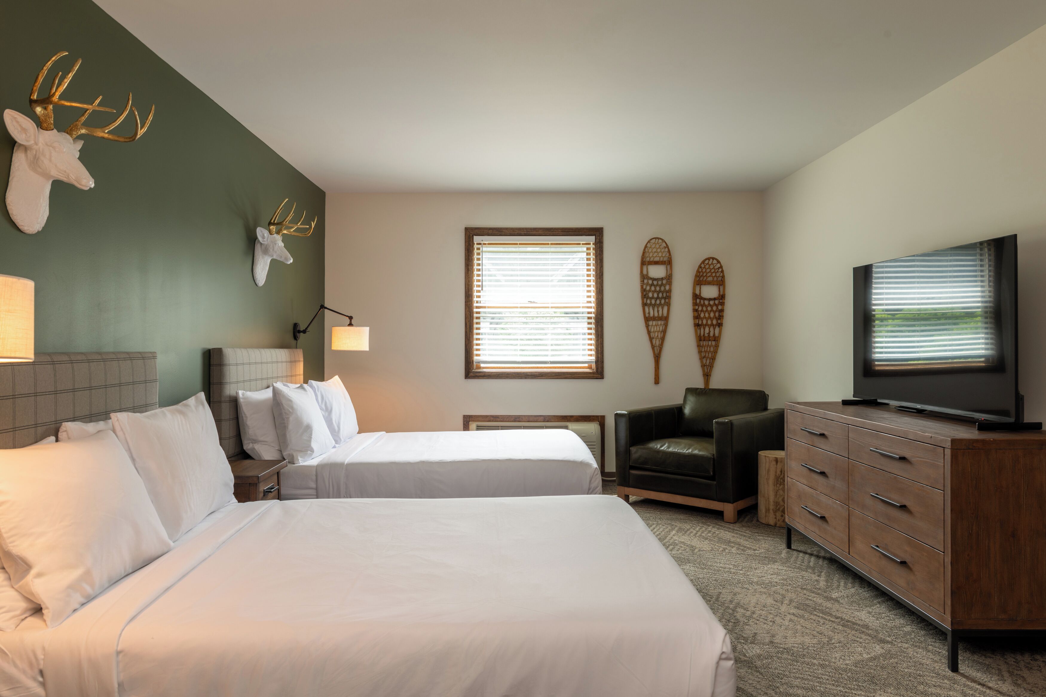 A hotel room with two beds, a television, a desk, and a chair.