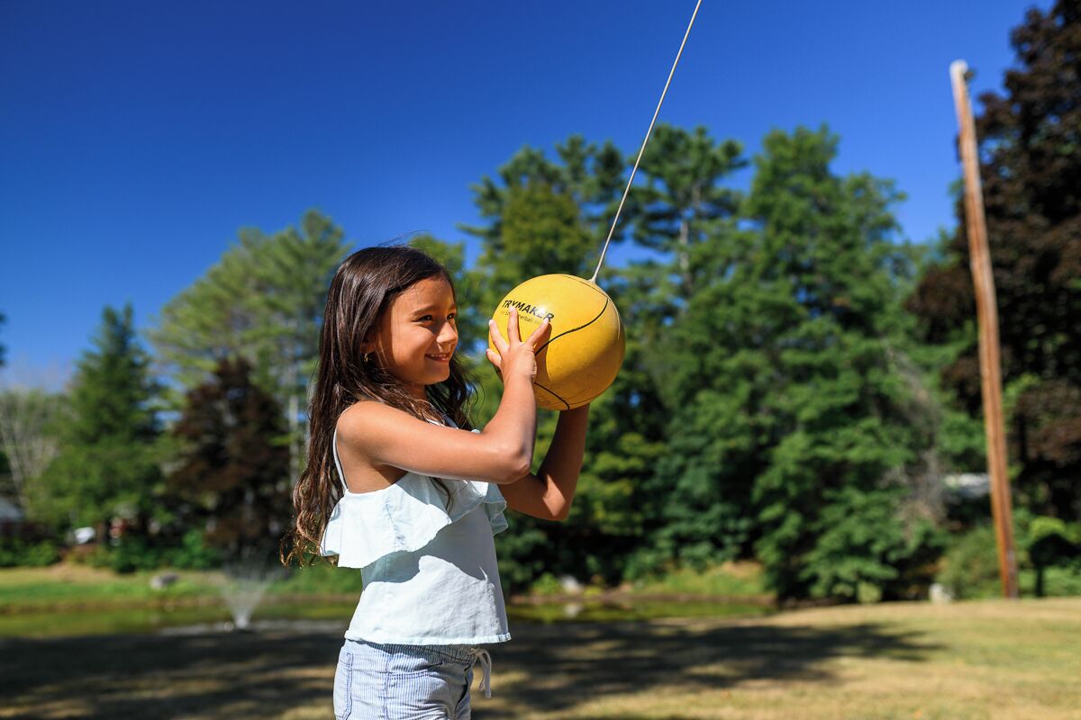 A person holding a yellow ball with a string, outdoors with trees and a clear sky in the background.