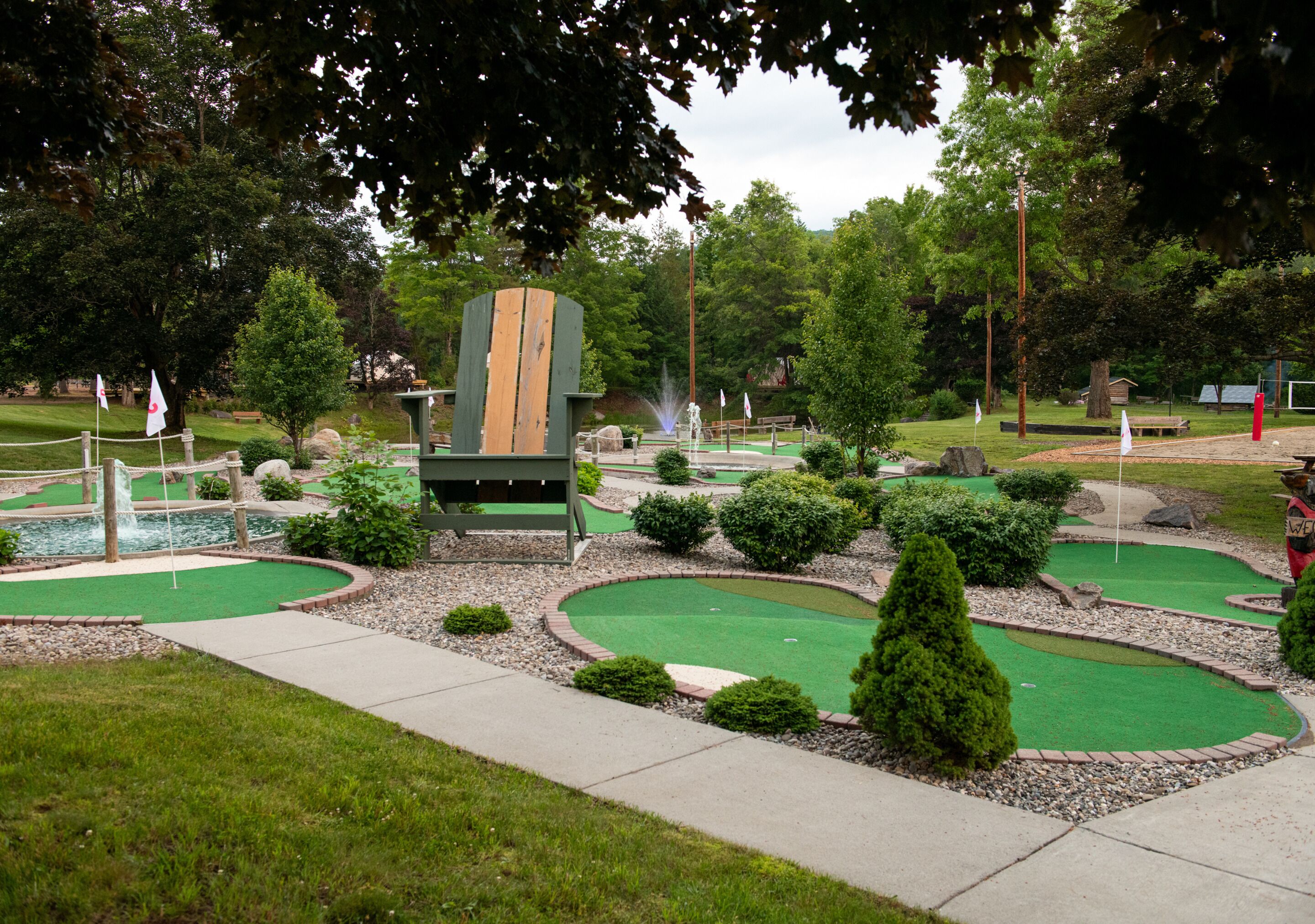A miniature golf course with multiple putting greens, a wooden structure, and surrounding greenery.