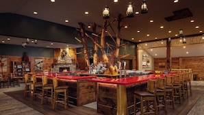 A bar area with a central island, wooden chairs, and a stone fireplace.
