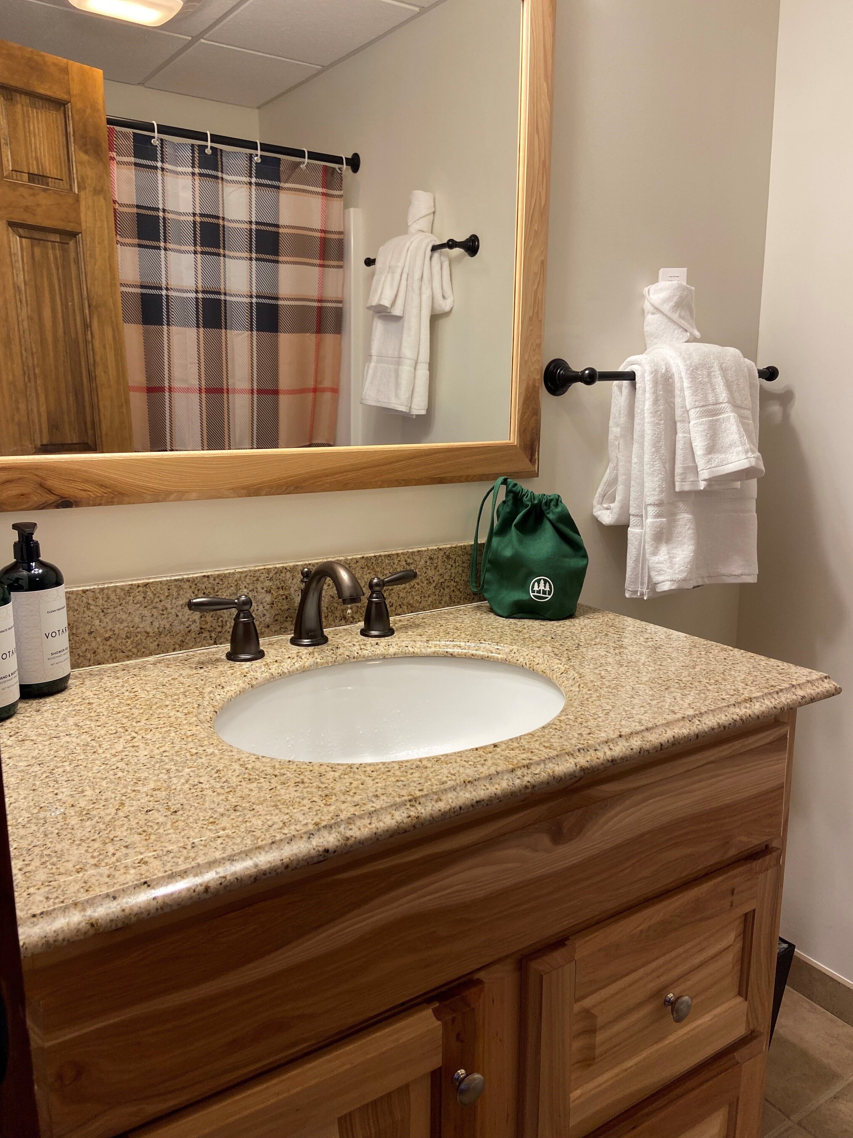 Un baño con encimera de granito, lavamanos blanco, tocador de madera, espejo y toallero con dos toallas blancas.