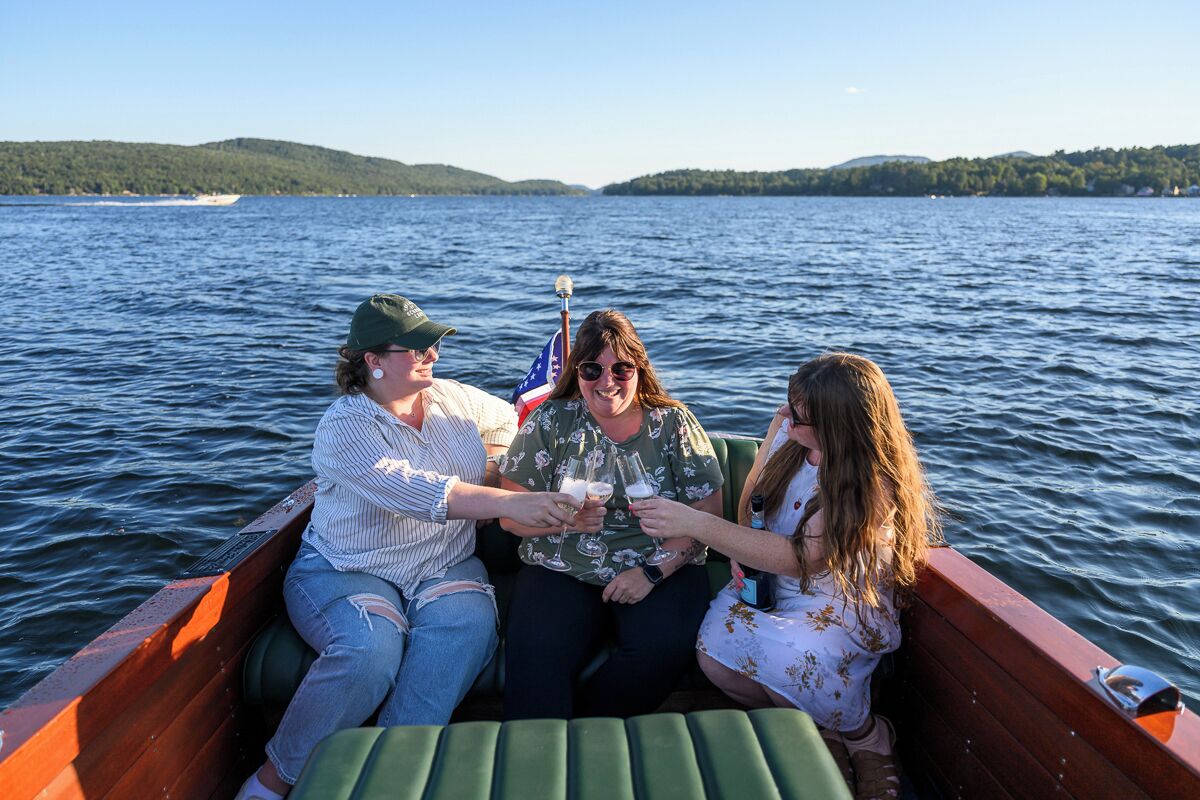 Three people in a boat on a lake with a flag, surrounded by water and hills.